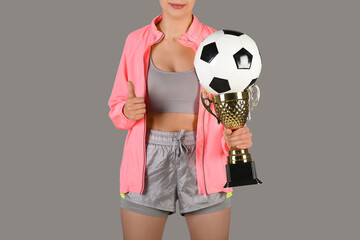 Female trainer with soccer ball and gold cup on grey background