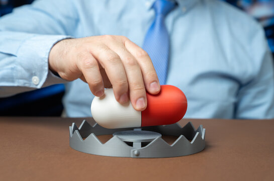 A man inserts a medication capsule into a trap. Drug addiction and medical collusion highlighting pharmaceutical abuse regulatory failure and healthcare ethics concerns.