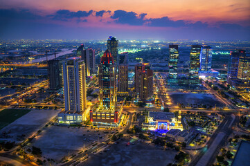 Skyline of Doha, Qatar, viewed at dusk with city lights, roads, and high-rise towers under a colorful evening sky.