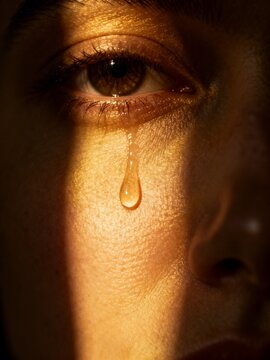 A tear drops from a sorrowful eye, a poignant moment captured in a close-up portrait, illuminated by soft light in a dim environment