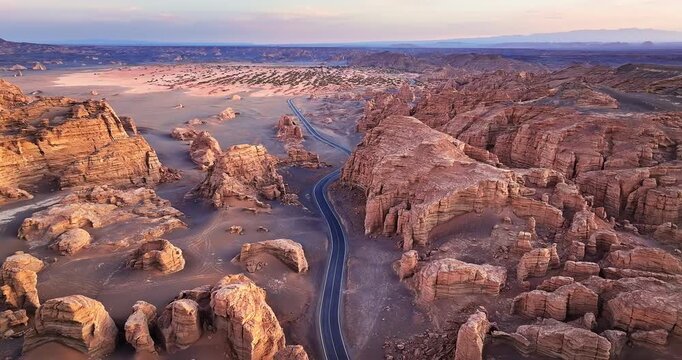 High angle view of a curved highway crossing the unique Yardang geological formations during a golden sunset in Xinjiang, China.