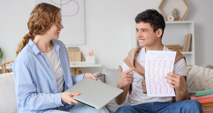Happy teenage boy showing results of school test to his mother sitting on sofa at home