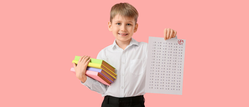 Happy boy with good results of school test and books on pink background