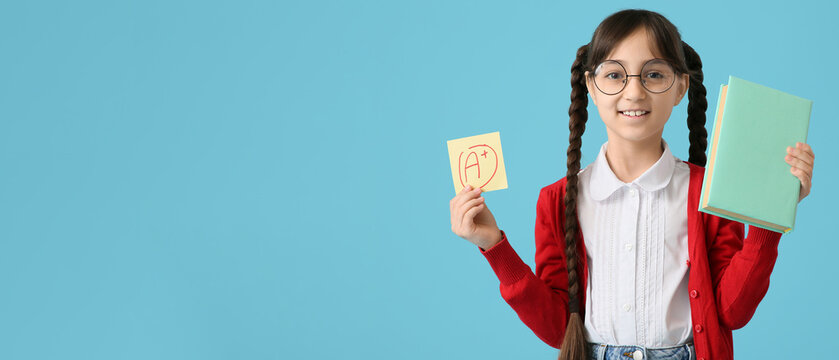 Happy schoolgirl holding book and sticky note with a-plus grade on blue background with space for text