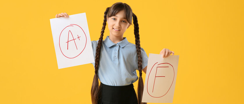 Happy schoolgirl holding papers with different grades on yellow background