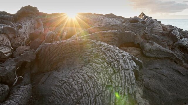 Golden sun flare shines through hardened lava formations on El Hierro, the low angle shot captures the rugged volcanic surface. Basaltic rocks glisten under the morning light