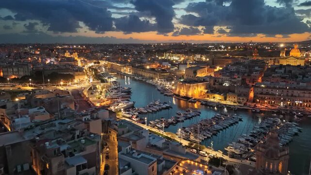 Sunset aerial panorama of Malta Three Cities and Grand Harbour, beautiful city lights reflecting in water with yachts at marina. Breathtaking twilight cityscape of Malta harbor with luxury yachts