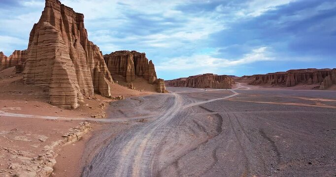 Aerial view of majestic Yardang landforms and winding dirt roads in the remote desert under a cloudy blue sky in Xinjiang, China.