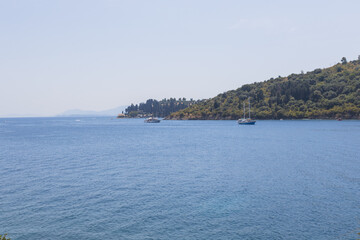 Scenic view of Mediterranean coastal landscape with white sailboat anchored in calm blue bay waters.