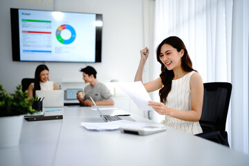 Fototapeta premium Celebrating professional success, a joyful business woman holding document containing exciting news or an approved document, receiving important mail at her modern office desk