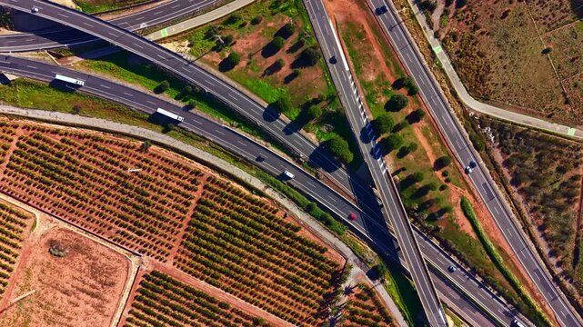 Traffic moves on multiple highways while vineyards and fields are visible in the landscape. Green trees line the roads in the countryside area.