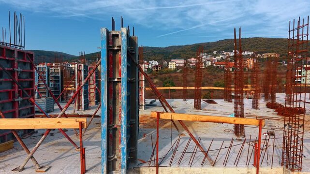 Numerous metal rebars and frames set on the roof of the unfinished building. Footage along the roof of the future hotel. Mountainous area with urban landscape in the backdrop.