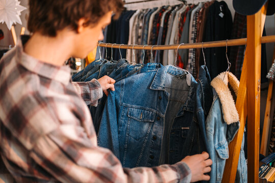 Teenage Shopper Scans Through Various Distressed Denim Coats Inside Cozy Store Environment