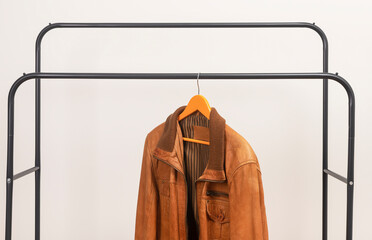 Brown leather jacket hanging on metal rack. Outerwear garment placed on wooden hanger. Menswear wardrobe piece suitable for autumn spring season.. © valiantsin