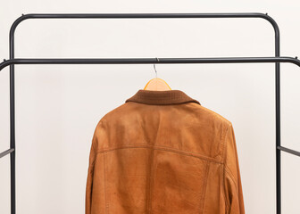 Brown leather jacket hanging on metal rack. Outerwear garment placed on wooden hanger. Menswear wardrobe choice for autumn spring season.. © valiantsin