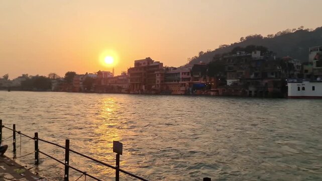 Scenic evening sunset over the Ganges River in Haridwar, India, with riverside buildings and hills silhouetted against a warm golden sky reflecting on sacred waters