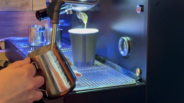 Barista preparing milk in a coffee machine for adding to coffee. Female hands are making coffee using professional metal machine in cafe. Barista is heating milk, whipping foam with frother, steam. 