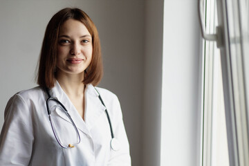 Positive female doctor in a white coat with a stethoscope on her neck in a hospital, portrait of a doctor.