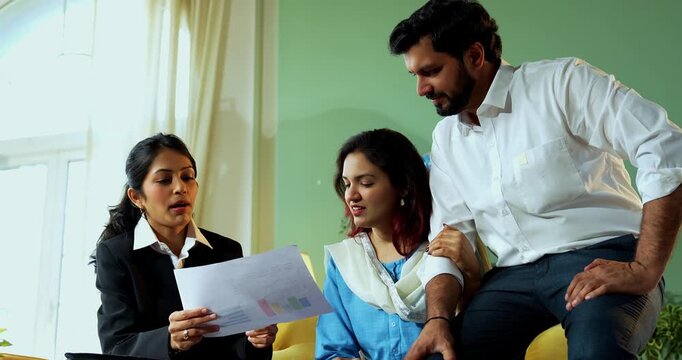 Indian young happy couple discussing financial or legal matters with female corporate consultant during home meeting while reviewing documents and planning their future security together.