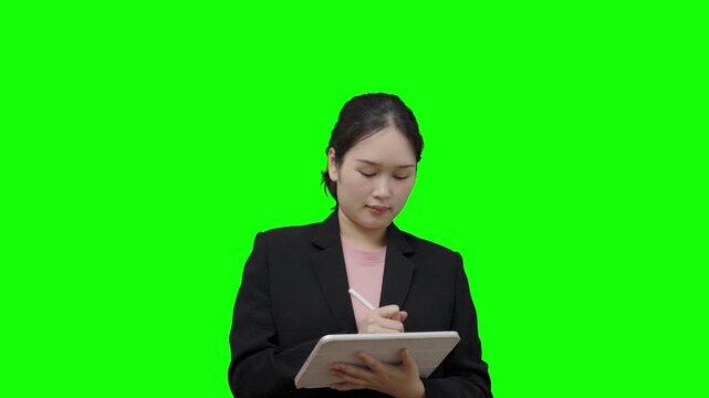 Asian businesswoman is using a digital tablet to take notes or analyze data, against a green background.