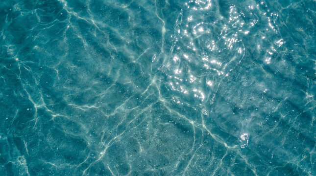 Ultra macro top view of crystal clear azure water with soft ripples and bright sunlight reflections. A serene and fresh texture of a tropical ocean surface, perfect for summer or nature themes.