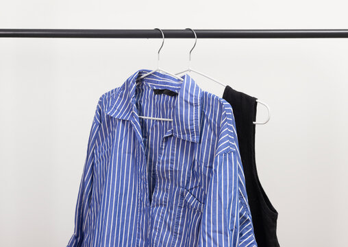 Wrinkled blue striped women shirt hanging on rack. Garment loosely placed on hanger below rail. Female wardrobe clothing showing messy unpressed fabric.