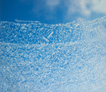 window galss with frozen snowflakes and blue sky behind