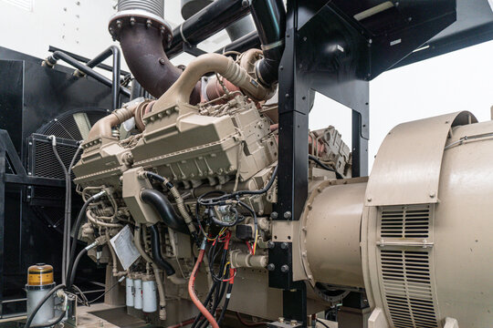 Heavy-duty generator sits ready for power needs. Metal pipes, wires, and robust housing show industrial strength. Engine mounted beside cooling unit indicates high performance