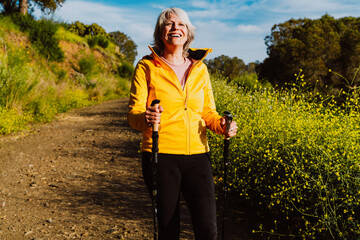 Active senior woman hiking on outdoor trail using trekking poles