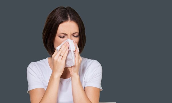 Brunette girl sneezing in a tissue on color background