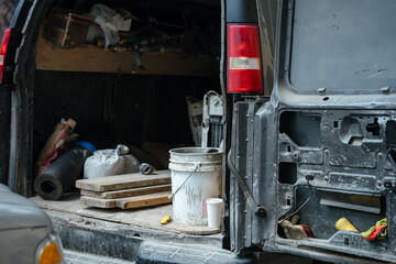 An open work van reveals construction tools, buckets, and materials inside the cargo area. The image represents manual labor, maintenance, and service work.
