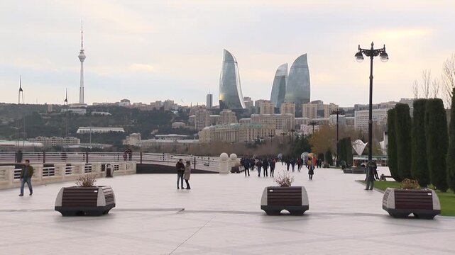 Baku's promenade with people and a panoramic view of the city, a view of the TV Tower and the Flame Towers on a cloudy day