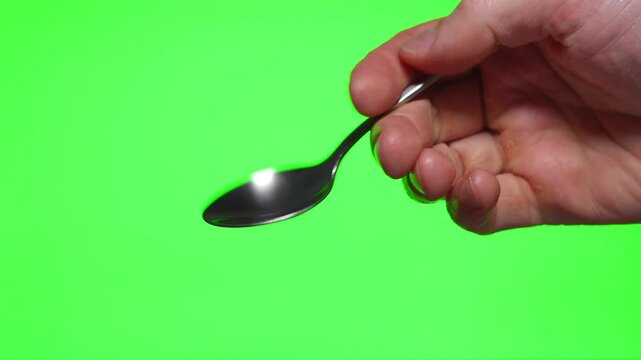 Metal teaspoon in hand on green background