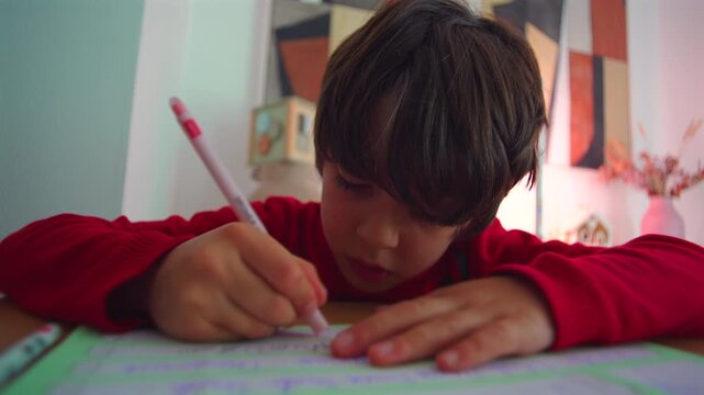 Young boy writing homework with pencil at desk, focused expression while practicing letters and numbers in colorful family home interior
