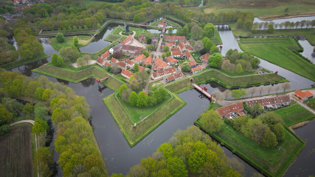 Aerial view of a star fort with red-roofed buildings surrounded by a moat and lush green trees, creating a striking contrast, Bourtange, Groningen, Netherlands.