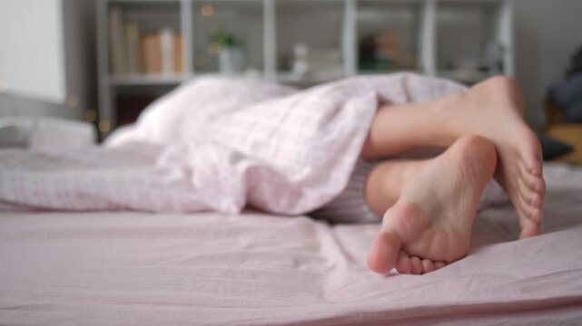 Female feet under blanket flat lay. Female beautiful feet with red pedicure on the bed. Top view on the sleeping woman legs under pink blanket. white quilt in early morning.