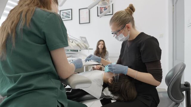 Professional dentist and nurse use micro applicator brush to apply liquid bonding adhesive on teenage boy tooth preparing oral cavity for composite filling in stomatology clinic room.