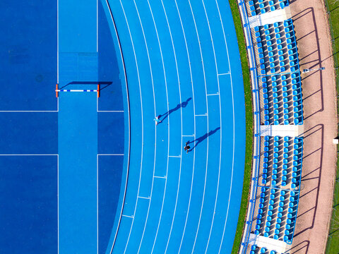 Aerial view of the vivid blue running track curving gracefully beside rows of empty stadium seats, painted in matching hues of blue, Warsaw, Poland.