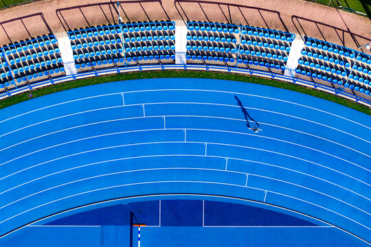 Aerial view of the blue running track curving gracefully around the stadium seating, creating a vibrant contrast against the green grass, Warsaw, Masovian Voivodeship, Poland.