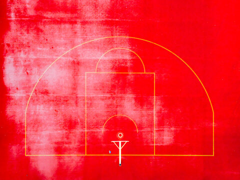 Aerial view of a vibrant red basketball court with crisp yellow lines creating a striking contrast, a geometric dance from above, Warsaw, Masovian Voivodeship, Poland.