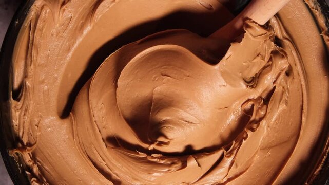 4K Landscape View of a Wooden Spoon Scooping Smooth Orange Speculoos Cookie Butter from a Large Tub. Top Down View