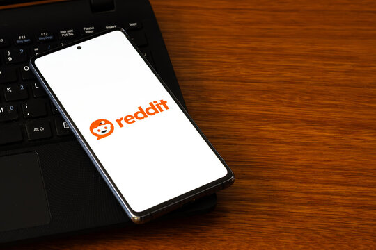 Punta Arenas, Chile &ndash; March 05, 2026: A smartphone screen displaying the Reddit logo and orange mascot, resting on a black laptop keyboard over a wooden desk