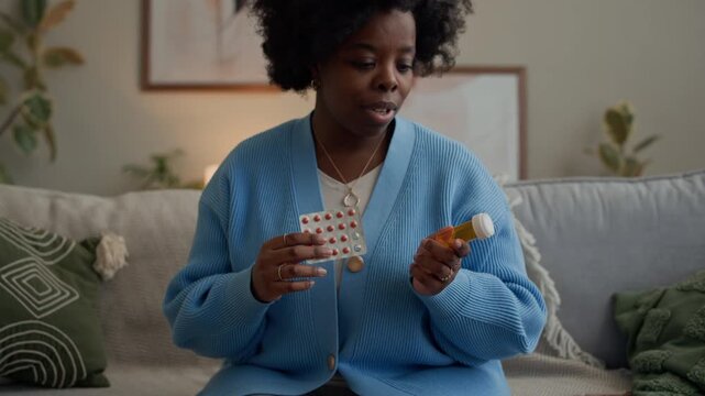 Handheld shot of young adult Black woman consulting about contraceptive pills during video call on wireless laptop while sitting on couch in living room