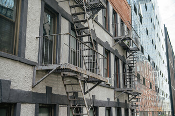Series of metal fire escapes run along a textured residential facade in Manhattan, New York City. Urban architectural details emphasize safety structures and classic apartment design.