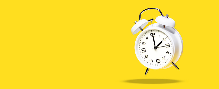 White bell alarm clock hovering over yellow background. 2 to 3 clock concept isolated. daylight savings time change concept
