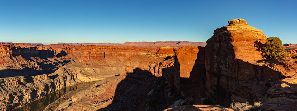 This scenic panorama of Canyonlands National Park near sunset features the Colorado River flowing through this colorful, rugged landscape under a vibrant blue sky.