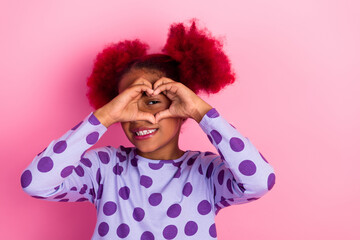 Young girl pink hair makes a heart shape with her hands pink background wearing a purple polka dot...