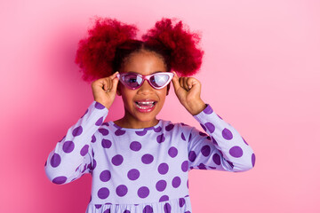 Young girl with pink hair wears purple polka dot dress and pink sunglass smiles against pink background © deagreez