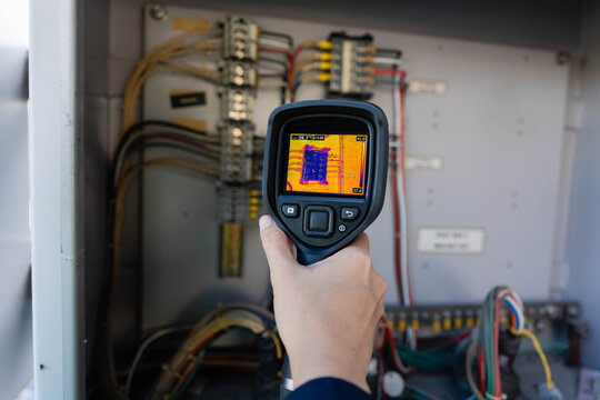 Close-up thermal camera infrared inspection monitoring of electrical panel; handheld imager checks terminal block temps to find loose connections and reduce downtime risk onsite