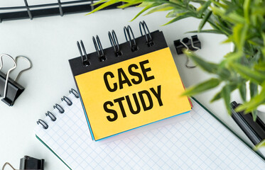 CASE STUDY text on a yellow note in a notebook on an office desk with binder clips and green leaves for business research and analysis concept.